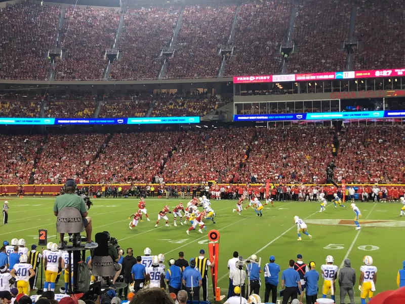 A full Arrowhead Stadium at night, stands packed in red, the Chargers and Chiefs lined up at midfield