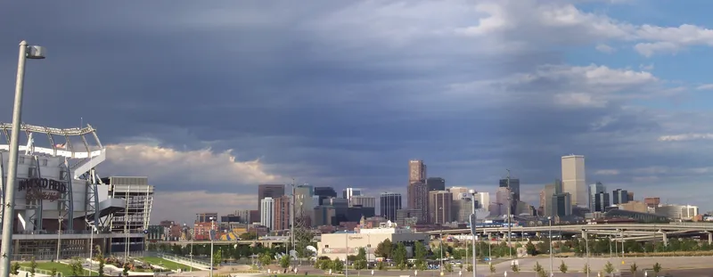 Panoramic view of the Broncos' stadium at left with the downtown Denver skyline rising beyond it under a stormy sky