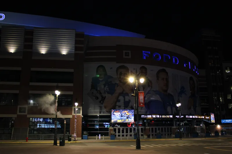 Ford Field's exterior at night with the stadium name lit and Lions player murals along the facade