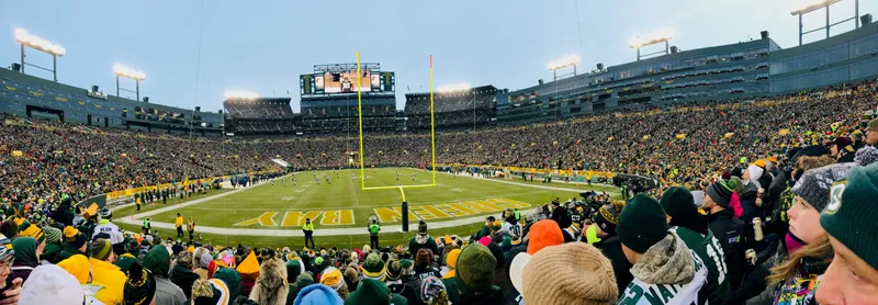 Panoramic view of a full Lambeau Field bowl from the stands during a December game, fans in green and gold winter gear