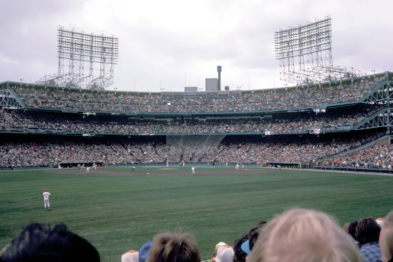 Metropolitan Stadium's packed grandstand and light towers seen from the outfield seats during a daytime game