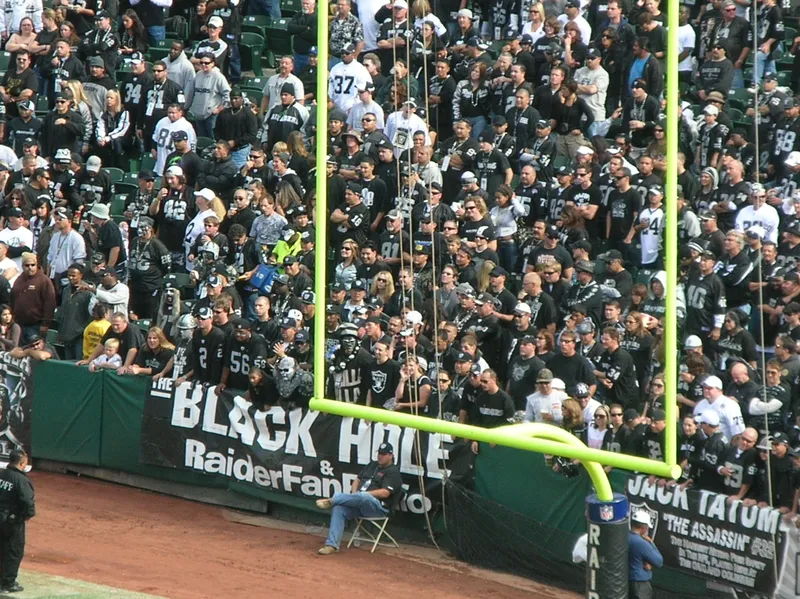 Raiders fans dressed in black packed into the end-zone seats behind a Black Hole banner and a goalpost at the Oakland Coliseum