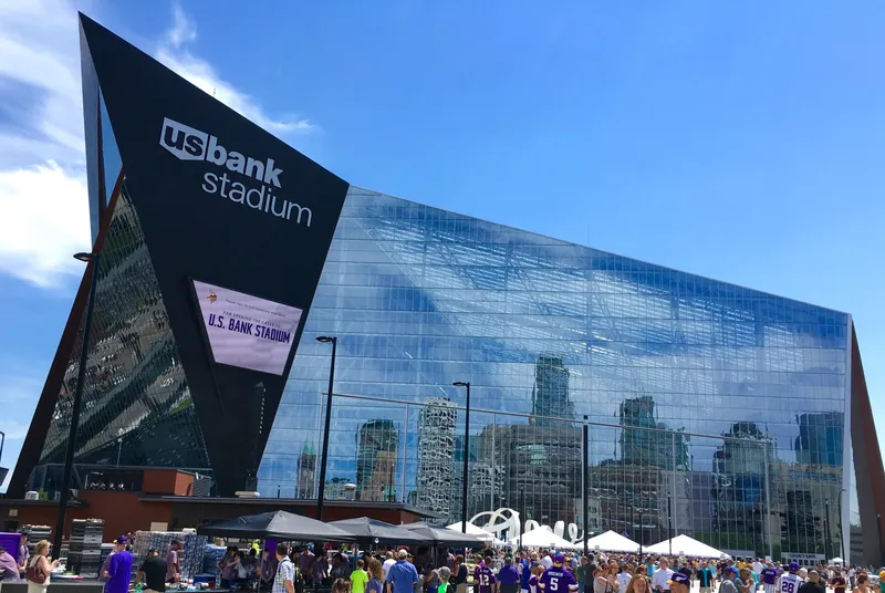 The glass west facade of U.S. Bank Stadium reflecting the Minneapolis skyline, with fans on the plaza