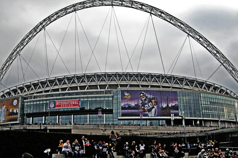 Wembley Stadium exterior under its arch, dressed with NFL International Series banners as fans arrive